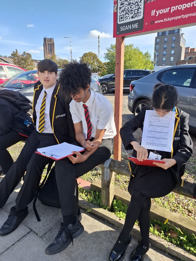 Three students sat down in Liverpool city centre during their geography fieldwork trip